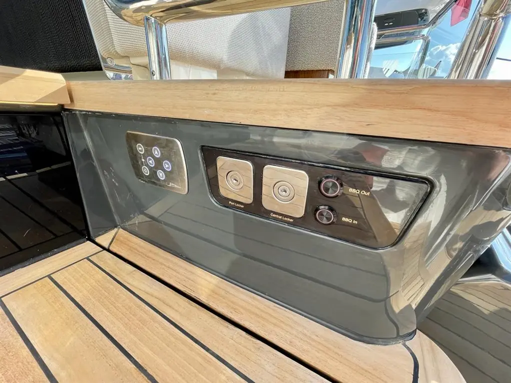 Control panel on a yacht featuring buttons for BBQ in/out, central locker, and a port locker, set against wooden decking.